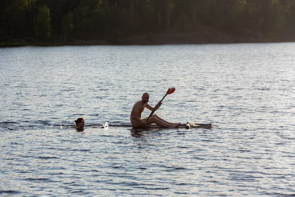swimming woman pushes a raft with a man on a lake