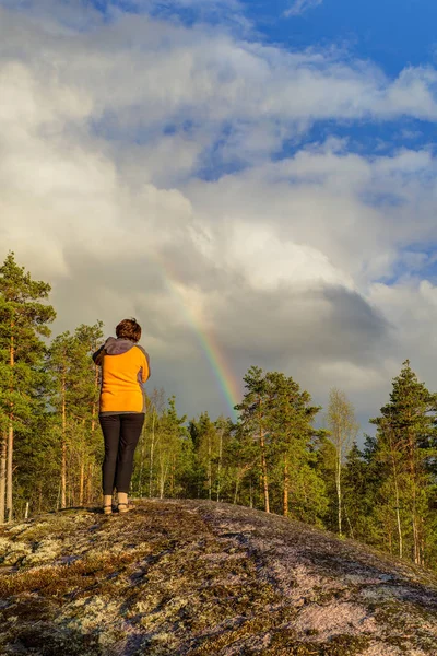 woman photographing a rainbow in the forest