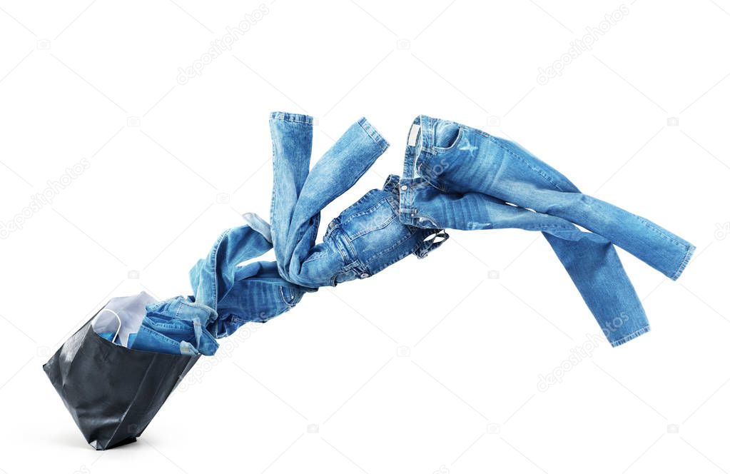 Denim clothes flying out of a black bag isolated on white backgr