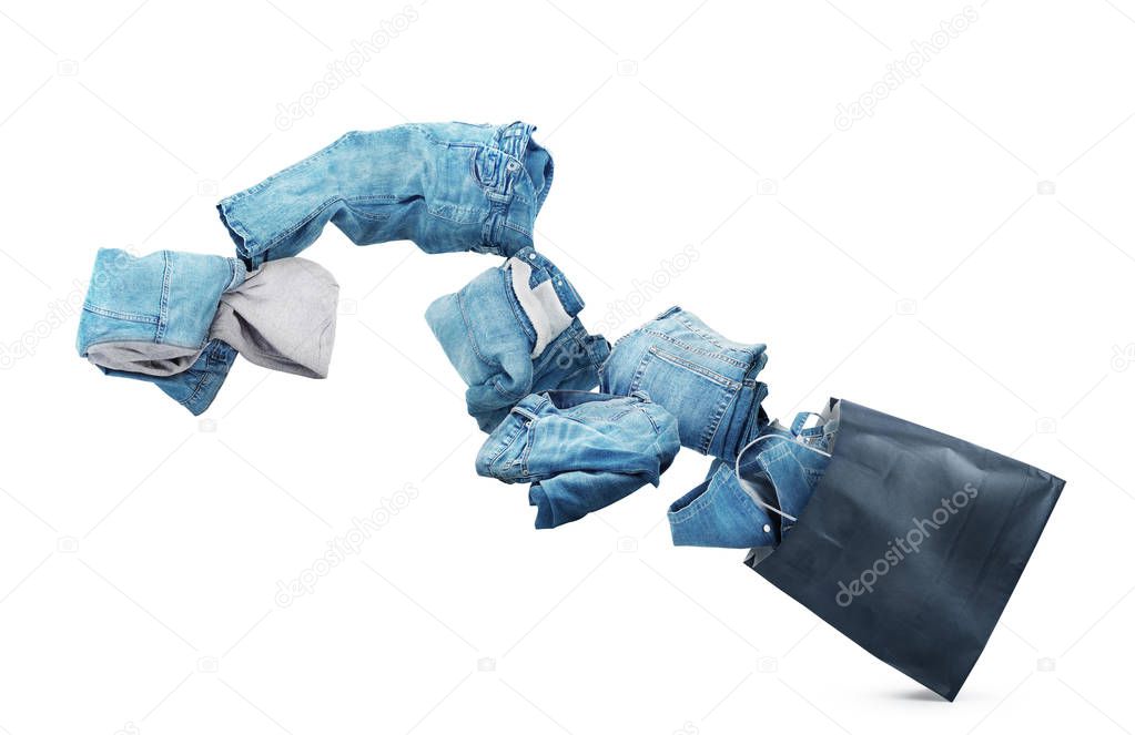 Denim clothes flying out of a black bag isolated on white backgr