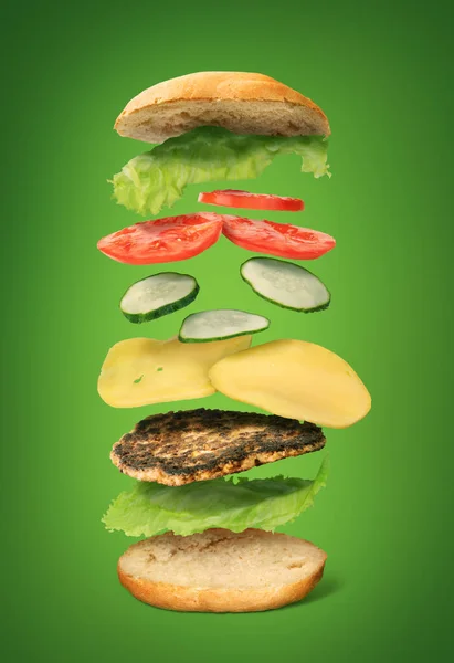 Burger ingredients flying on a green background — Stock Photo, Image