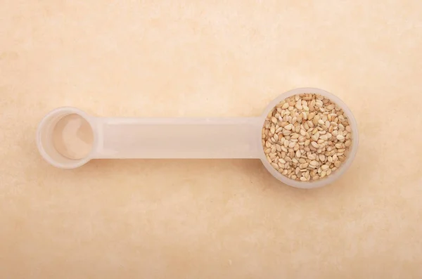 Sesame in measuring spoon on brown background — Stock Photo, Image