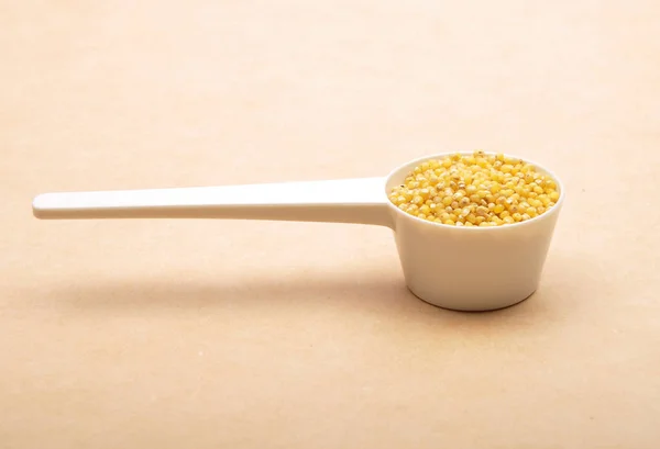 Raw millet in  measuring spoon on brown background — Stock Photo, Image