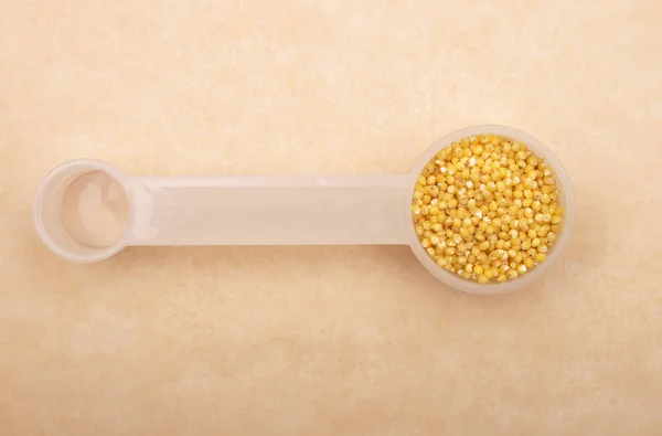 Raw millet in  measuring spoon on brown background — Stock Photo, Image