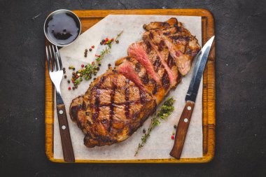 Sulu ızgara büyük striploin biftek otlar ve tuz ile süslenmiş. Çatal ve bıçak yanında kesme tahtası