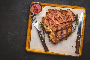 Etli otlar ve tuz ile süslenmiş büyük t-bone biftek ızgara. Çatal ve bıçak yanında kesme tahtası 