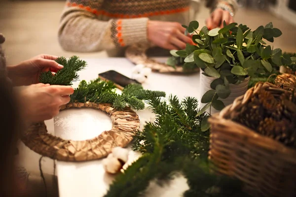 木製テーブルの上のモミの枝と装飾的な果実のクリスマス リースを作る花屋手のビューをトリミング — ストック写真