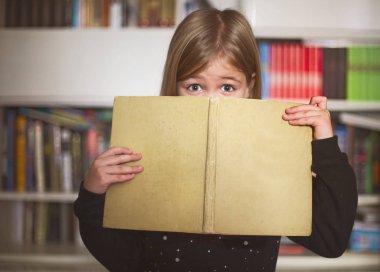 Kitap ve kameraya gülümseyen sevimli küçük kız öğrenci portresi