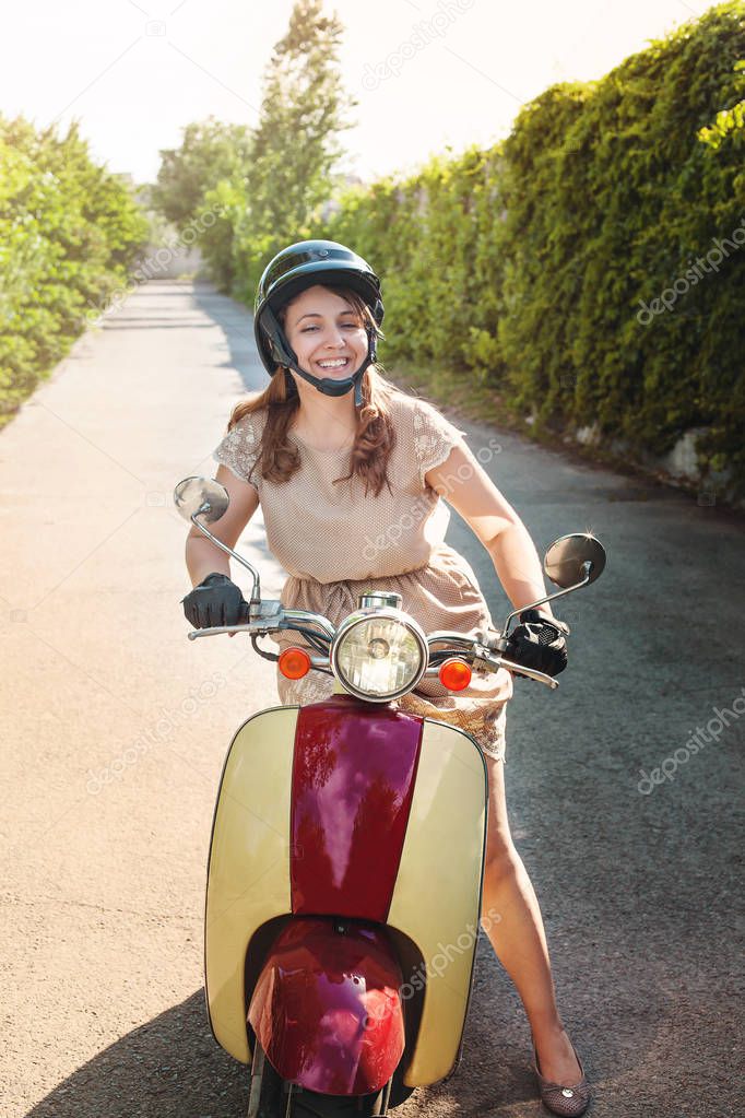 Young woman wearing dress driving a scooter on a countryside road 