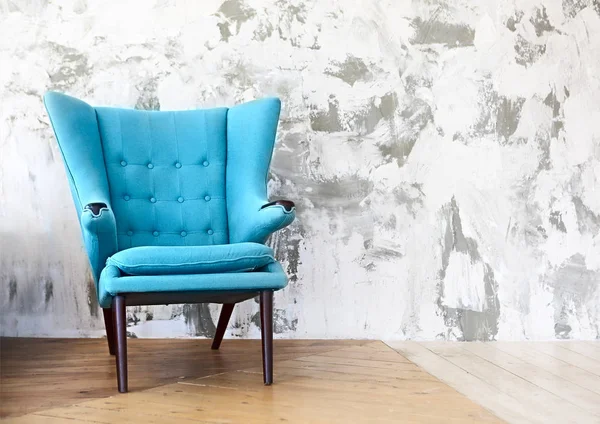 One blue armchair against a white and gray wall and wooden floor. Copy space
