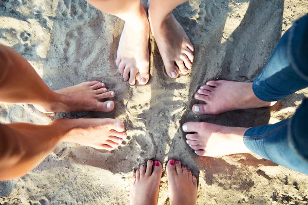 Top view image of feet of the female friends standing on the sand beac