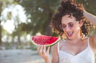 Güzellik gülümseyen kıvırcık kadın pembe güneş gözlüğü takıyor ve sahilde karpuz yeme
