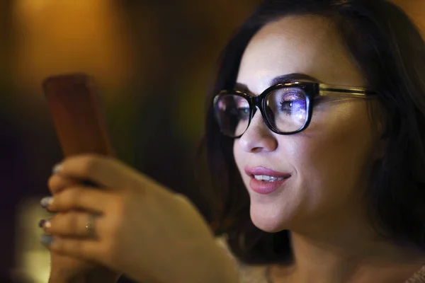 Woman using smartphone inside restaurant at night wearin glasses