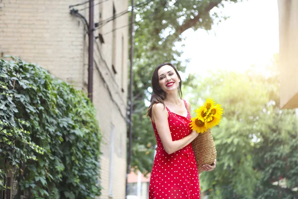 美丽的年轻女子在红色的波尔卡点礼服举行篮子向日葵 — 图库照片