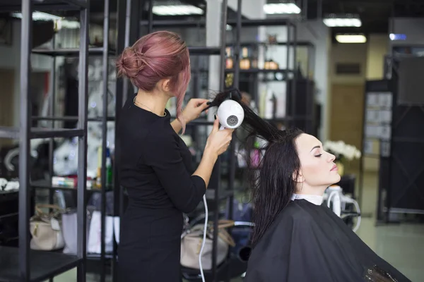 Professional hairdresser preparing to give a haircut to her beautiful cheerful female client combing her hair. Beauty industry service