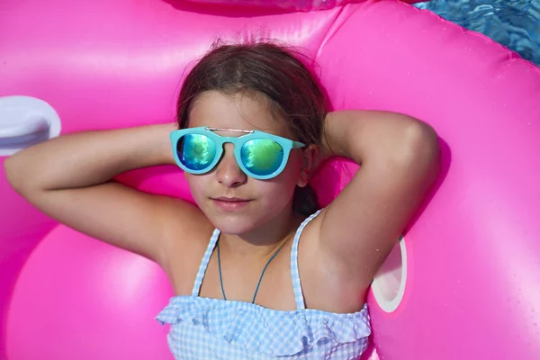 夏にプール パーティーを楽しんでいるフラミンゴの膨脹可能な水泳フロートでサングラスをかけている少女の肖像画 — ストック写真