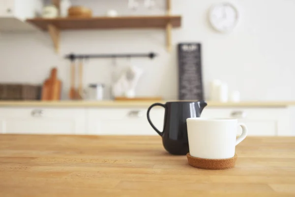 Wooden table with mug and milk jug with blurred kitchen background, copy space