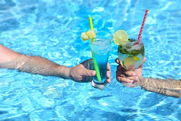 在游泳池里喝着酒精鸡尾酒的年轻夫妇莫吉托和蓝色泻湖 — 图库照片