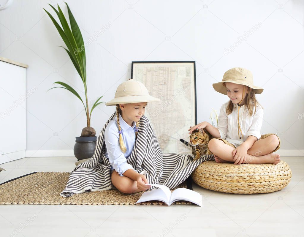 Two little girls are playing at home to travelers with bengal cat wearing vintage style clothes. Childhood, fantasy, imagination