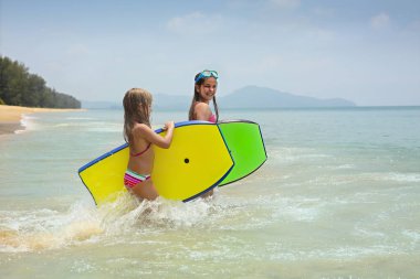 Tropikal okyanus kumsalda oynarken sörf tahtaları ile küçük kızlar
