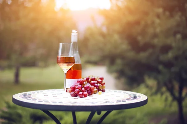 Una copa y una botella de vino de rosas en el viñedo de otoño en mármol t —  Fotos de Stock