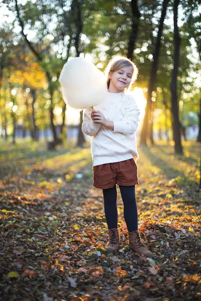 Маленька мила дівчинка з бавовняними цукерками на фоні осіннього парку — стокове фото