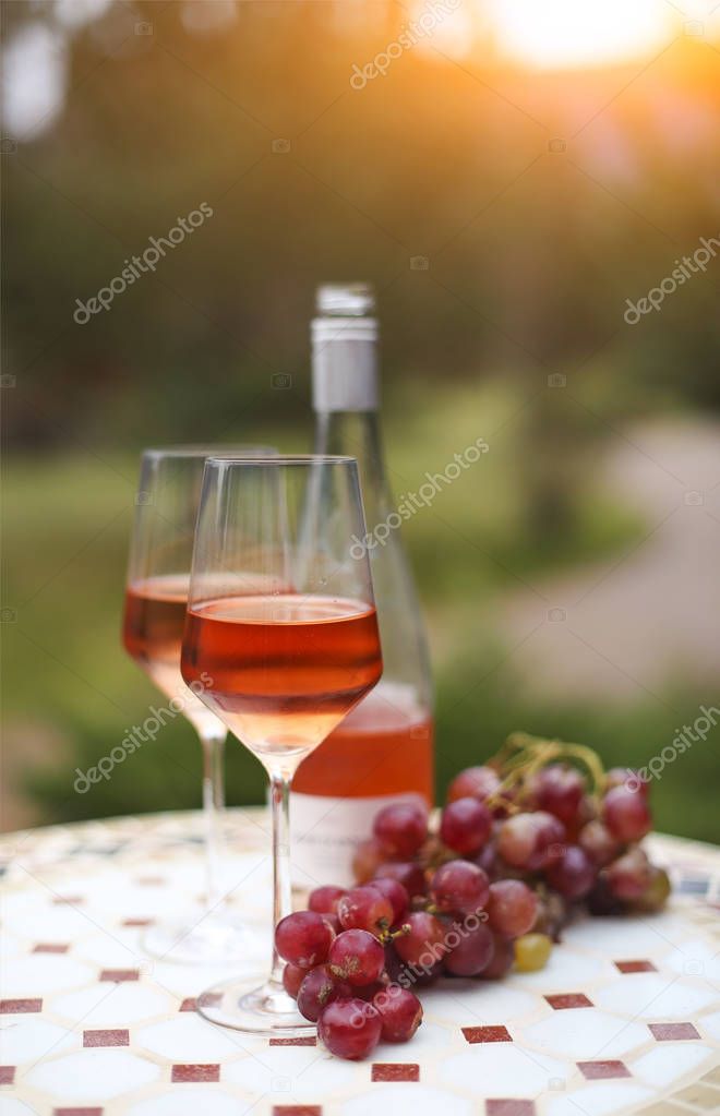 Two glasses and bottle of rose wine in autumn vineyard on marble