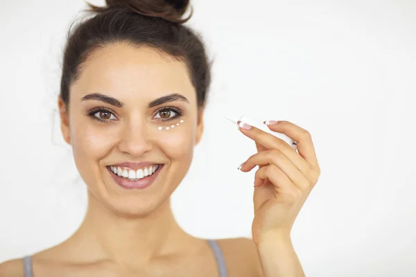 Young woman applying eyes cream on perfect skin