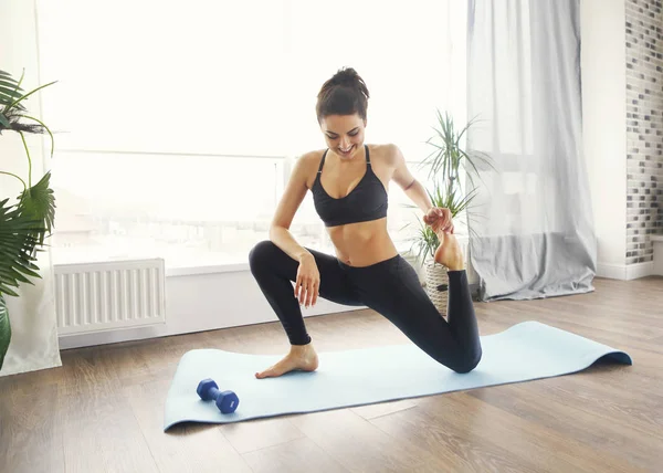 Smiling woman in sportswear exercising on fitness mat and in liv — Stock Photo, Image