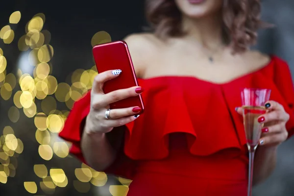 Ευτυχισμένο κορίτσι με κόκκινο φόρεμα κρατώντας το τηλέφωνο και το ποτήρι σαμπάνιας σε — Φωτογραφία Αρχείου