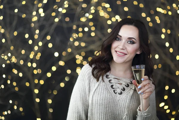 Femme souriante dans le pull avec une coupe de champagne sur les lumières — Photo