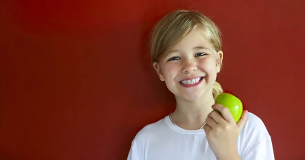 Felice bambina bionda con mela verde vicino al muro rosso — Foto Stock