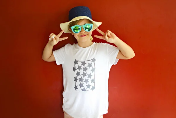 Pretty emothional child wear a hat and sunglasses on a red backg — Stock Photo, Image