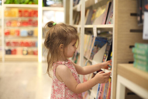 Little cute child picking books from the bookshelf 