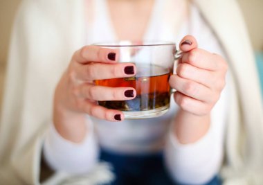 Evde dinlenirken cam bardakta aromalı bitki çayı tutan sıradan bir kadın yüksek açılı.