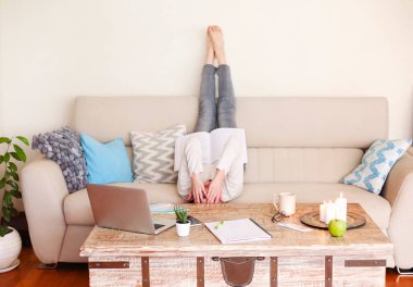 Arka planda, rahat oturma odasındaki projede çalışırken koltukta uzanmış, ayakları havada profesyonel edebiyat okuyan, tanınmamış, çıplak ayaklı genç bir kadın var.