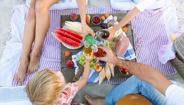 Küçük çocukları olan mutlu ve sağlıklı bir ailenin yaz günü kumsalda piknik yaparken meyve suyu şişeleriyle tezahürat etmesinden.