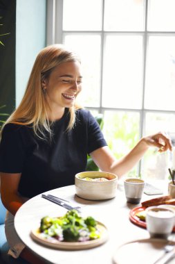 Lokantada masada otururken bir fincan taze kahveyle gülümseyen mutlu genç bayan.