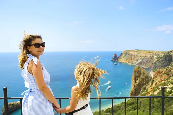母と少女がフェンスの横に立って 晴れた日には澄んだ空と青い水で岩だらけの海の海岸の絵のように美しい景色を眺める — ストック写真