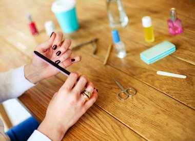 Manikür yapmak ve tırnaklarını törpülemek için çeşitli aletlerle ahşap masada oturan sıradan giysili, tanınmamış bir kadının yüksek açılı yan görüntüsü