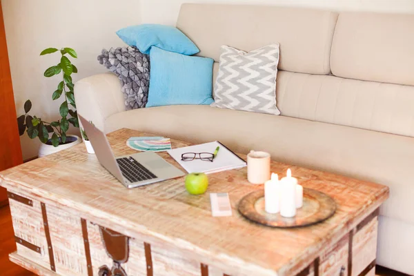 Interior of contemporary living room with cozy sofa and wooden table with laptop and papers placed near burning candles and cup of coffee during remote work from home