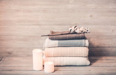 Pamuklu kumaş ve havlu gibi bitmiş ürünlerin yanında şeffaf kahverengi şişeyle bembeyaz mumlar yakarak.