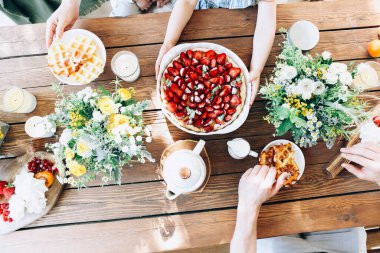 Tahta masada oturan, waffle ve çilek yiyen ve güneşli bir sabah kahvaltısı yapan tanınmamış aile manzarası.
