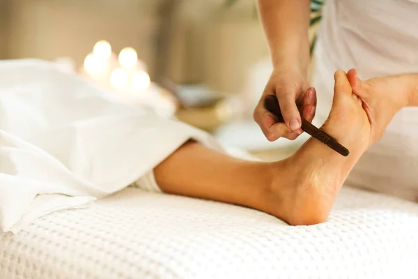 Unrecognizable therapist using foot file to make massage to anonymous customer during work in spa salon