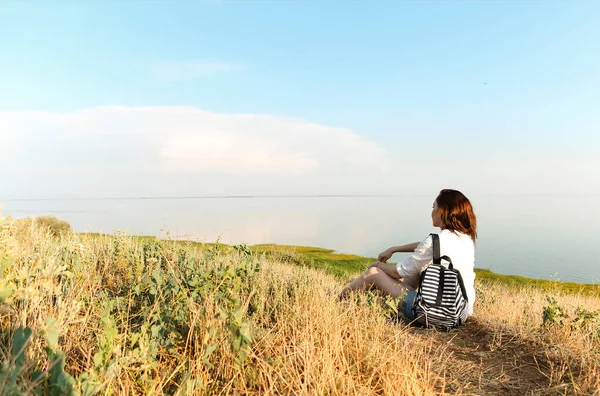 丘の上に草の上に座って夏の日没の間に素晴らしい景色を賞賛認識できない女性旅行者の側面図 — ストック写真