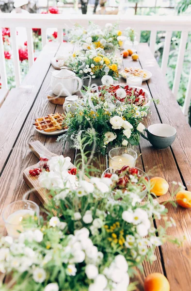 晴れた日には田舎の花の花束と木製のテーブルに並べられたおいしいイチゴケーキと自家製ワッフルのトップビュー — ストック写真
