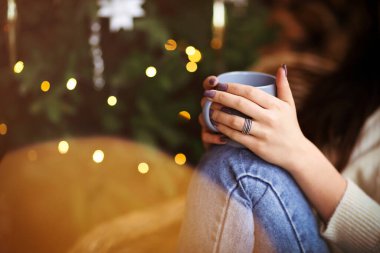 Noel ağacının ışıl ışıl arka planında dinlenirken aromatik sıcak içeceği koklayan...