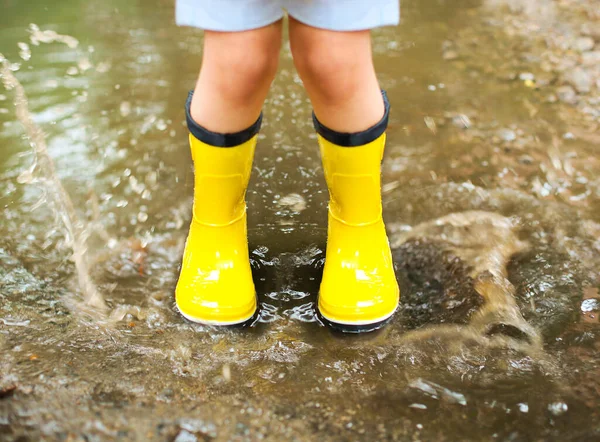 小さな女の子身に着けています黄色のブーツとコートジャンプで雨の日 — ストック写真