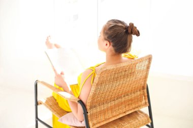 İç çamaşırlı sakin bir kadının oturma odasındaki hasır koltukta oturması ve hafta sonu dinlenirken ilginç bir hikayenin keyfini çıkarması.