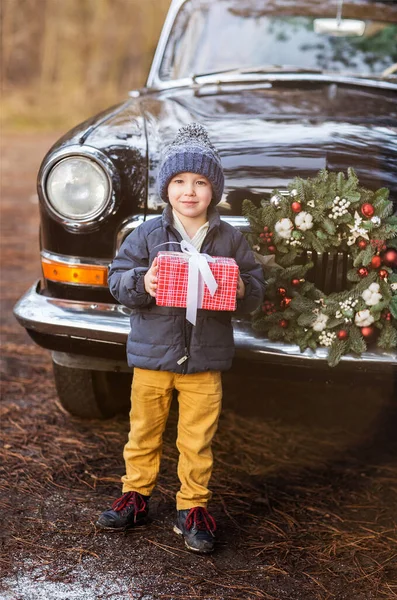 迷人的男孩站在复古的黑色轿车旁边 在冬季公园的屋顶上挂着箱子 — 图库照片